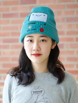 Woman with long dark hair wearing a hat and sweater with a brick wall in the background.