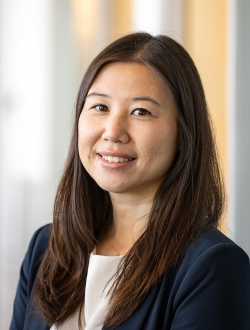 Smiling woman with long dark brown hair wearing a blue jacket over a white top.