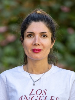 Woman with dark hair pulled back, wearing a white shirt with a green background.