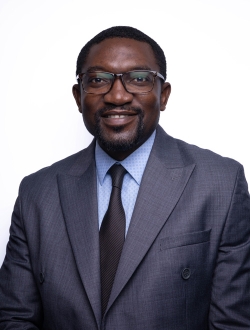 A man with short dark hair wearing glasses and a dark blue suit and tie.