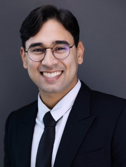 A person with short black hair wearing glasses and a suit and tie.