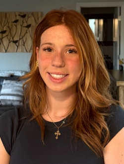 Smiling woman with long wavy light brown hair wearing a black t-shirt.