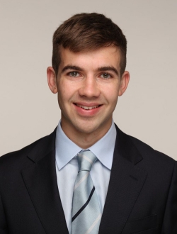 Smiling man with short brown hair wearing a suit and tie.