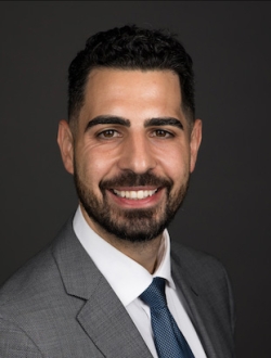 Smiling man with a short black beard and hair wearing a suit and tie.
