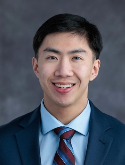 Smiling man with short black hair wearing a dark blue suit and tie.