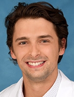 Smiling man with short black hair wearing a white lab coat.