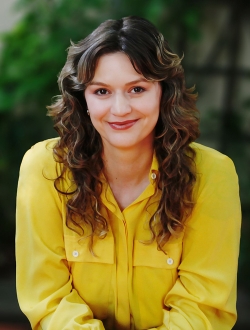 Woman with long wavy blonde hair wearing a yellow collard shirt.