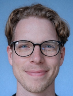 Man with short curly blond hair wearing glasses.
