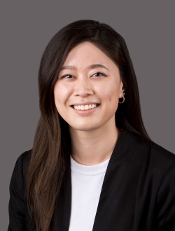 Smiling woman with long dark hair wearing a black jacket over a white top.
