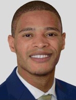 Smiling man with short dark hair wearing a navy blue suit and tie.
