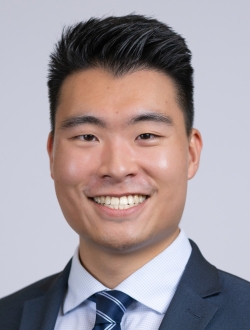 Smiling man with short black hair wearing a suit and tie.