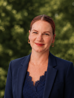 woman in blue blazer in front of trees