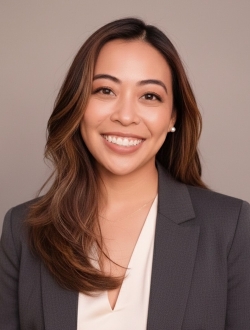 Smiling person with long brown hair wearing a blue jacket over a light colored top.