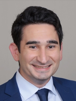 Smiling person with short black hair wearing a suit and tie.