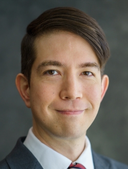 Person with short brown hair wearing a suit and tie.