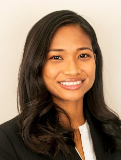 Smiling person with long dark brown hair wearing a dark jacket over a white shirt.