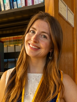 Smiling person with long brown hair standing in a library.