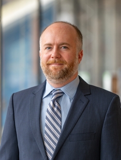 Person with short hair and beard wearing a suit and tie.