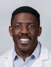 Smiling person with short black hair wearing a white lab coat over a light blue shirt.