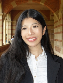 Smiling person with long black hair wearing a black jacket over a white shirt.