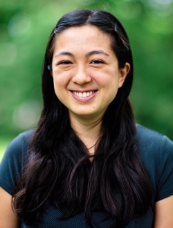 Smiling person with long black hair wearing a blue shirt.
