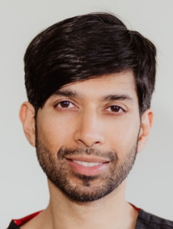 Smiling person with black hair and a short black beard wearing dark scrubs.
