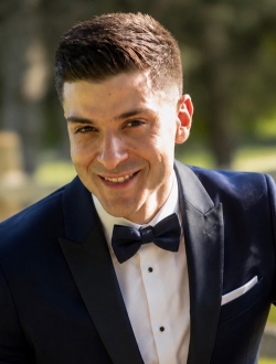 Smiling person with short dark hair wearing a tuxedo.