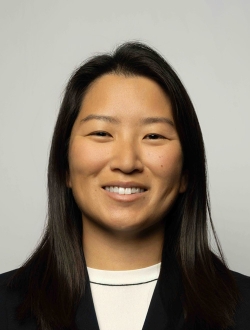 Smiling person with long black hair wearing a black jacket over a white shirt.