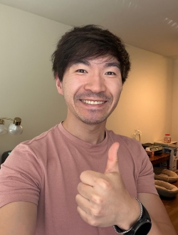 Person with short black hair, smiling and giving a thumbs up gesture.