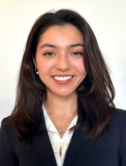 Person with long dark brown hair wearing a blue blazer over a white shirt.
