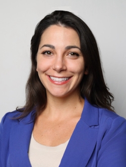 Smiling person with long black hair wearing a blue jacket over a white shirt.