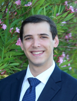 Smiling person with short dark hair wearing a navy blue suit and tie.