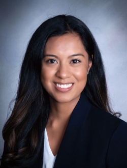 Smiling person with long black hair wearing a black jacket over a white shirt.