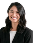 Smiling person with long black hair wearing a black jacket over a white top.