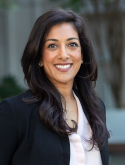 Smiling person with long black hair wearing a black jacket over a white shirt.