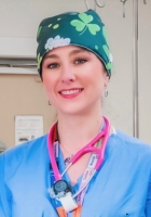 woman in blue scrubs and cap smiling at camera.