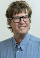 A man wearing a blue collard shirt and glasses