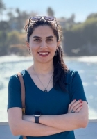 woman in a blue shirt smiling in front of water.