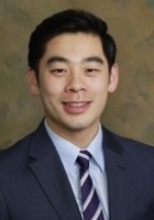 Man smiling with short black hair, wearing a dark suit, blue shirt and stripped tie