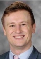 Smiling man with short light brown hair wearing a suit and tie.