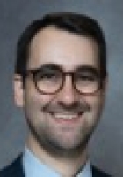 Smiling man with short dark brown hair and beard wearing glasses.