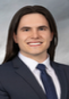 Smiling person with long dark brown hair wearing a suit and tie.