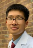 Man with short black hair wearing glasses and a lab coat.