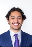 Smiling man with dark hair and mustache wearing a blue suite and tie.