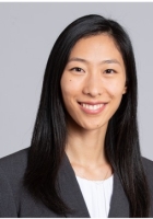 Smiling woman with long black hair wearing a dark jacket over a white top.