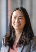 Smiling woman with long black hair wearing a gray jacket.