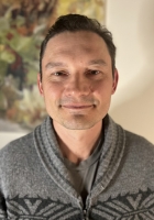 Man with short brown hair wearing a sweater.