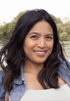 Smiling woman with long dark brown hair with trees in the background.