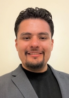 Man with short black hair and a goatee beard wearing a gray suit jacket over a black t-shirt.