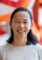 Smiling woman with long straight black hair wearing a light colored sweater with a colorful orange and yellow sculpture in the background..